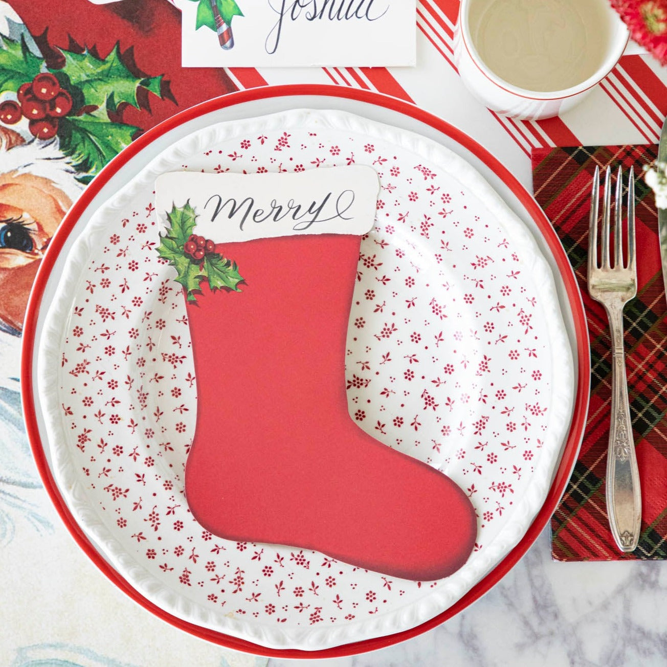 The Stocking Table Accent with &quot;Merry&quot; written on it, resting on a plate, on a Christmas themed table setting.