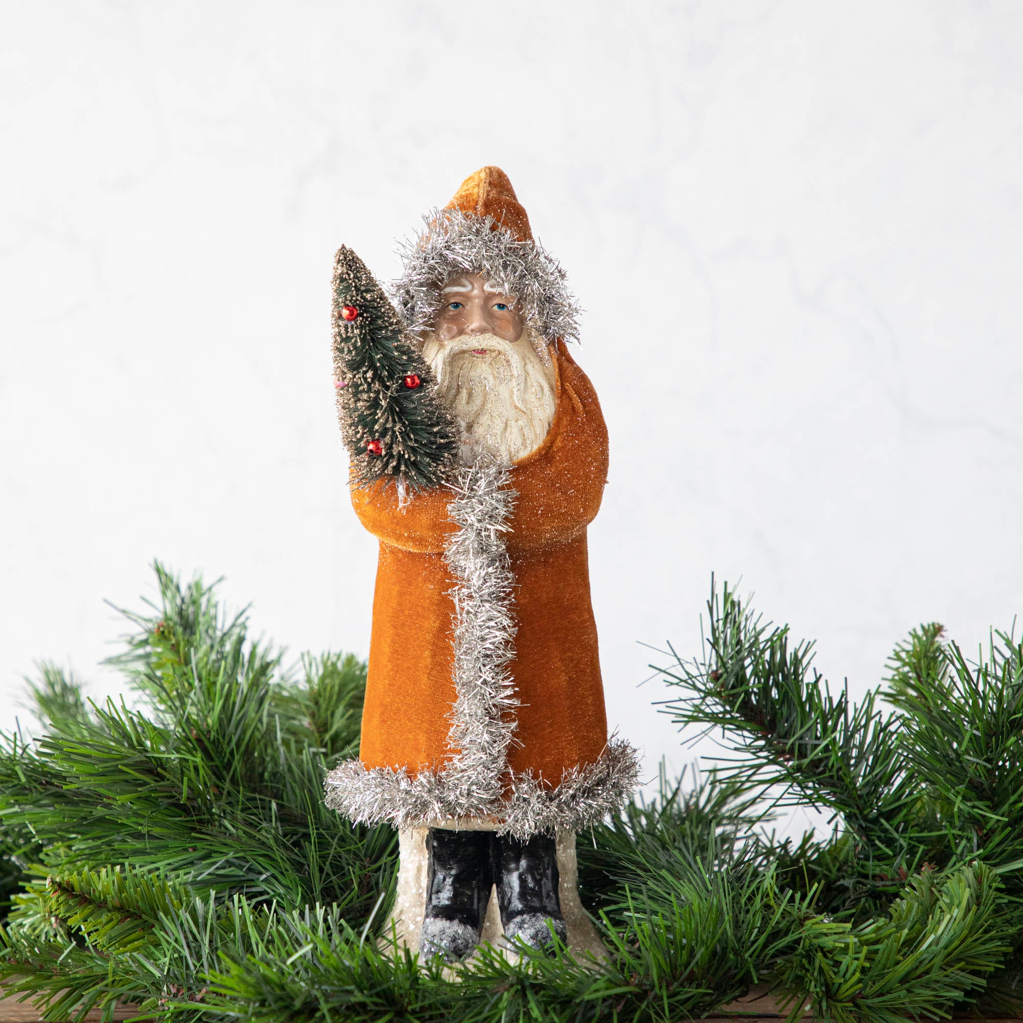 A 12" Velvet Belsnickle figurine with a gold velvet robe adorned with tinsel trimming and glitter, holding a tree.