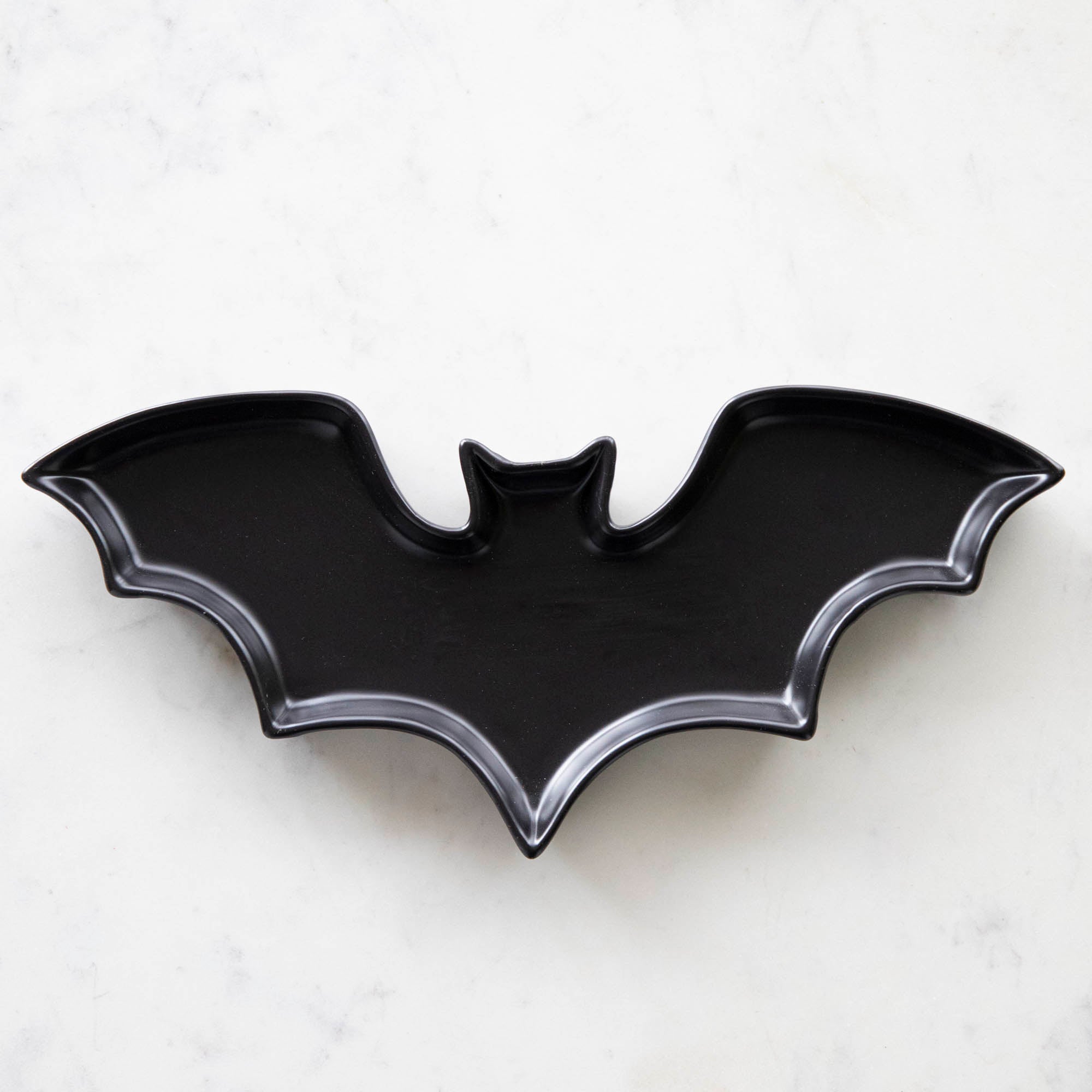 Black Stoneware Bat Shaped Plate on a marble table.