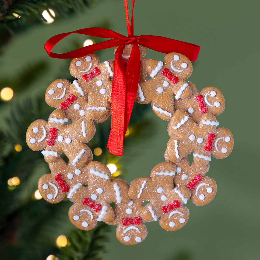 Gingerbread men ornament with a red ribbon on a Christmas tree background.
