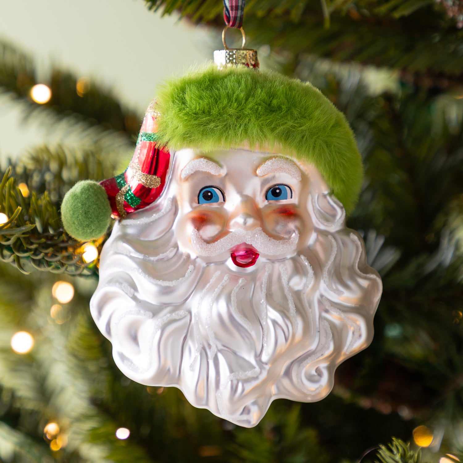 Christmas ornament of a Santa Claus face with a green hat on a tree..