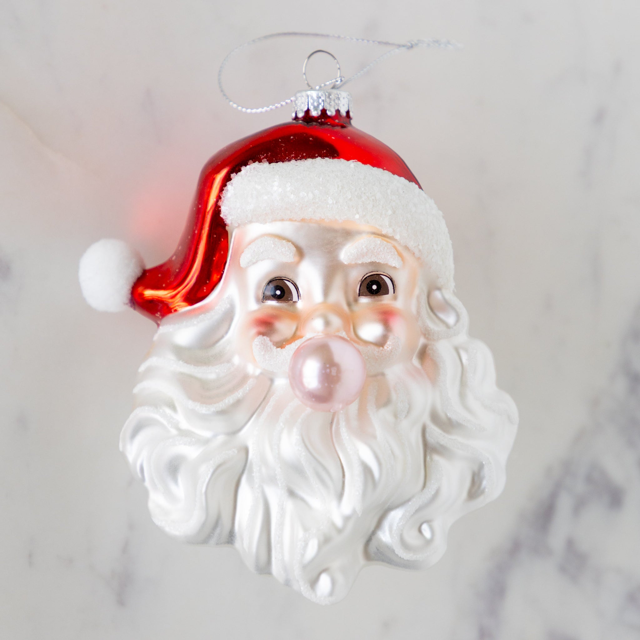 Glass ornament shaped like a Santa Claus head, showing Santa blowing a pink bubble.