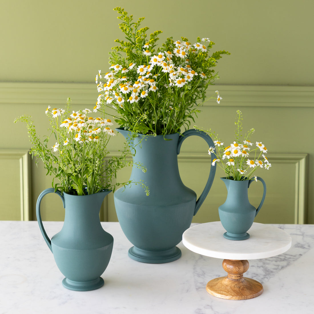 Three Toulouse Verdant Green Pitchers with flowers in them, on a marble table.