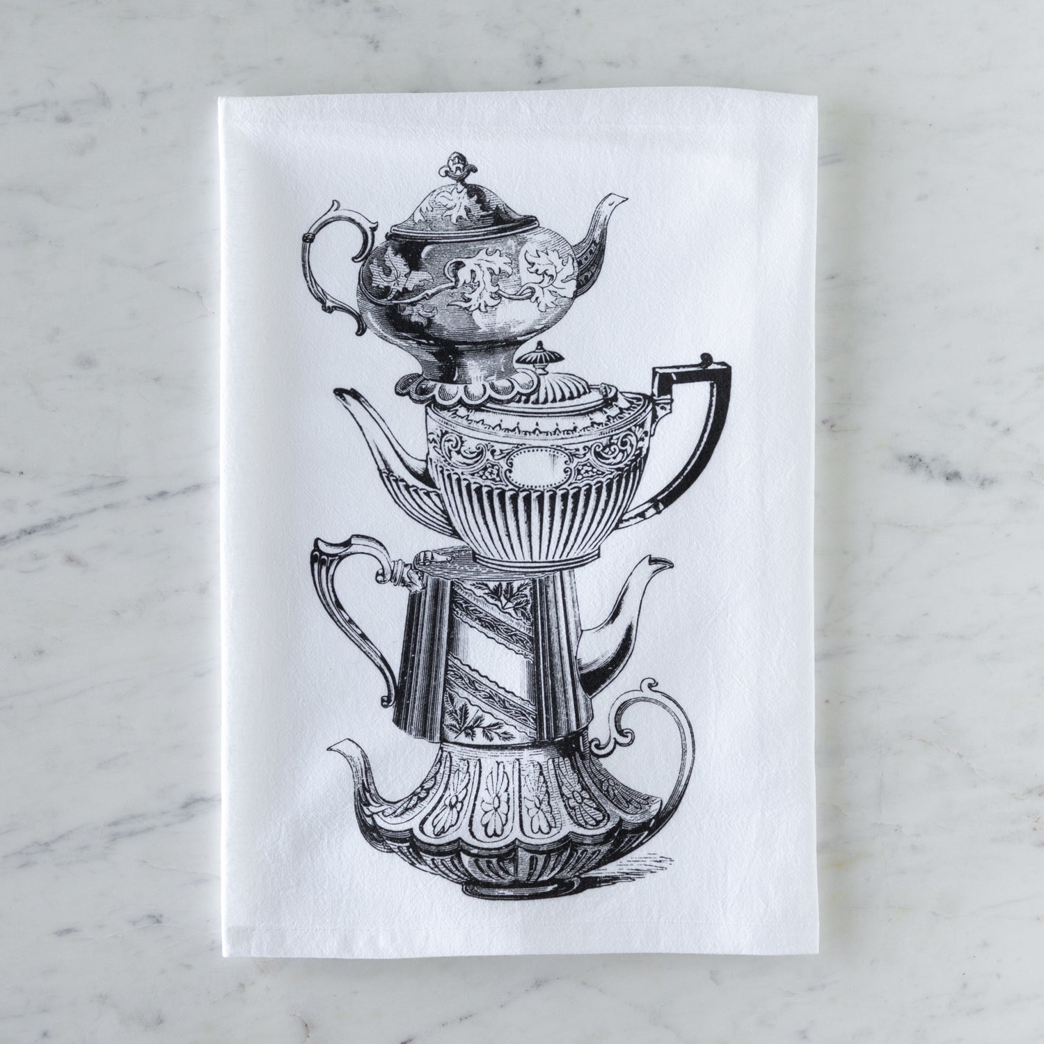 Tea towel with black and white illustration of vintage stacked teapots on a marble surface.