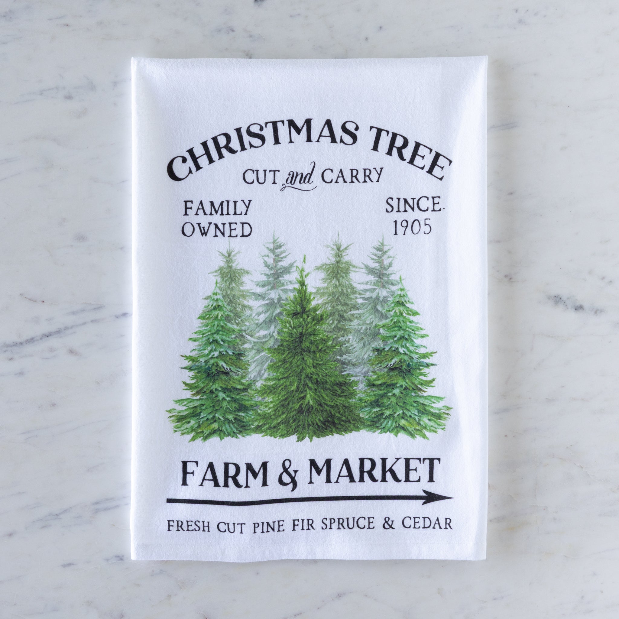 Tea towel with Christmas tree design and text on a marble surface.