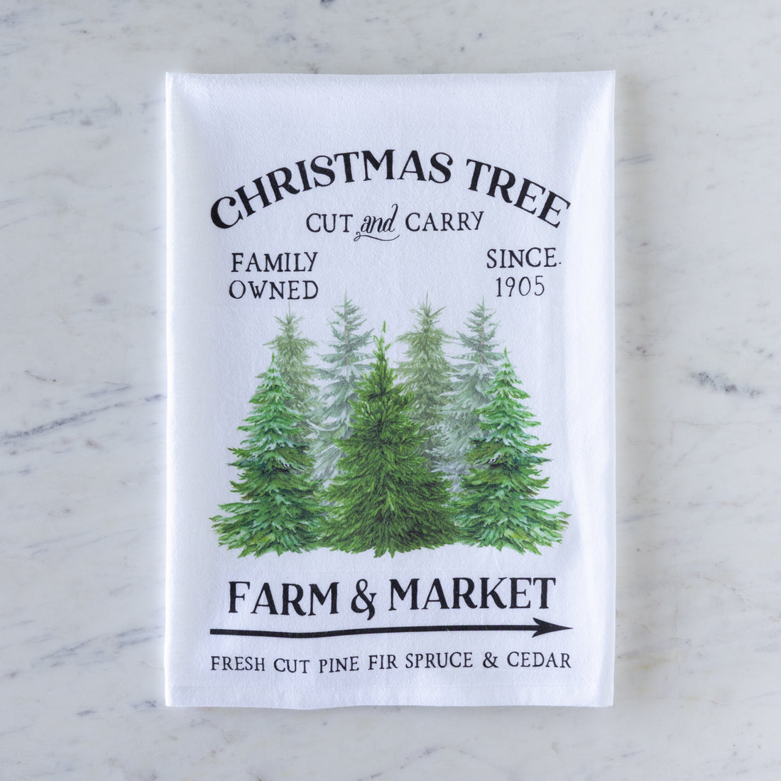 Tea towel with Christmas tree design and text on a marble surface.