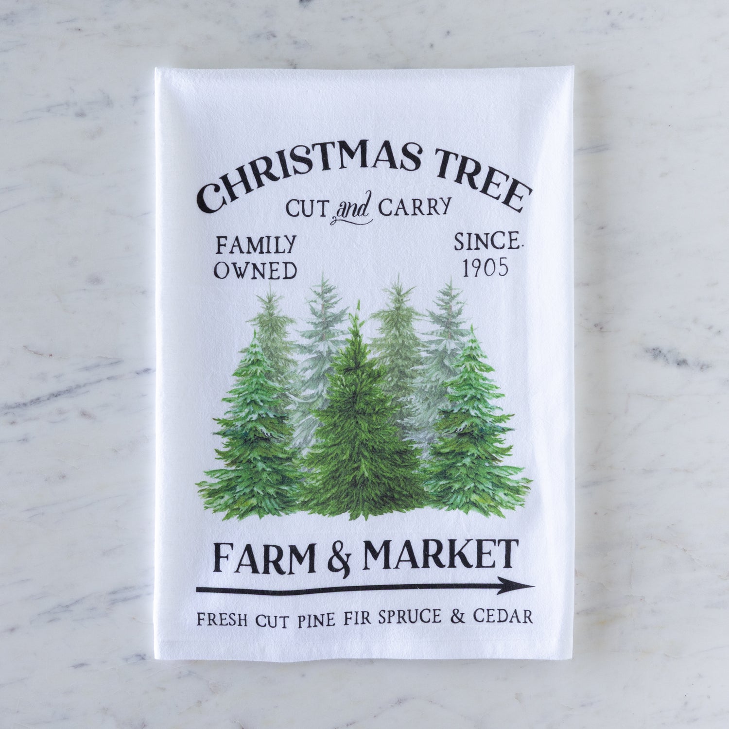 Tea towel with Christmas tree design and text on a marble surface.