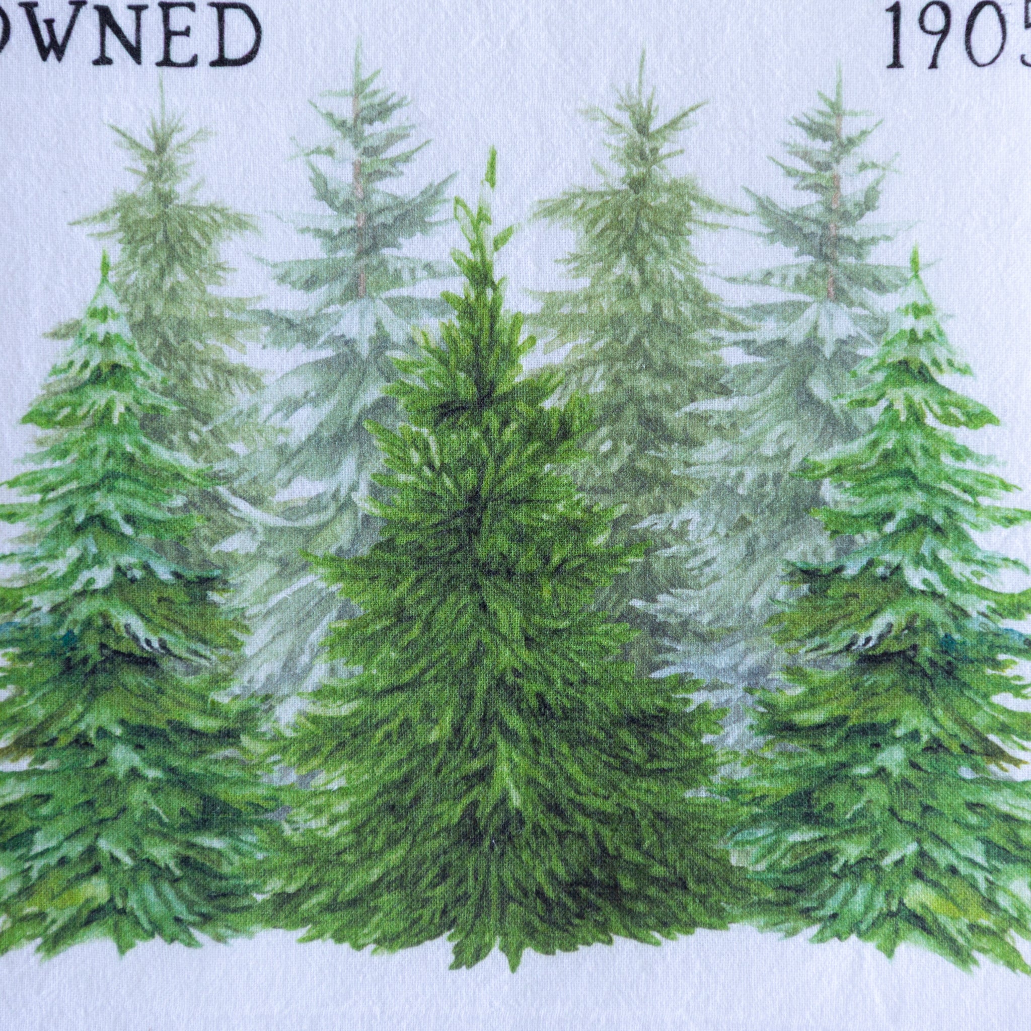 Close up of theChristmas Tree Farm & Market Cotton Tea Towel showing an illustration of snow-covered pine trees.