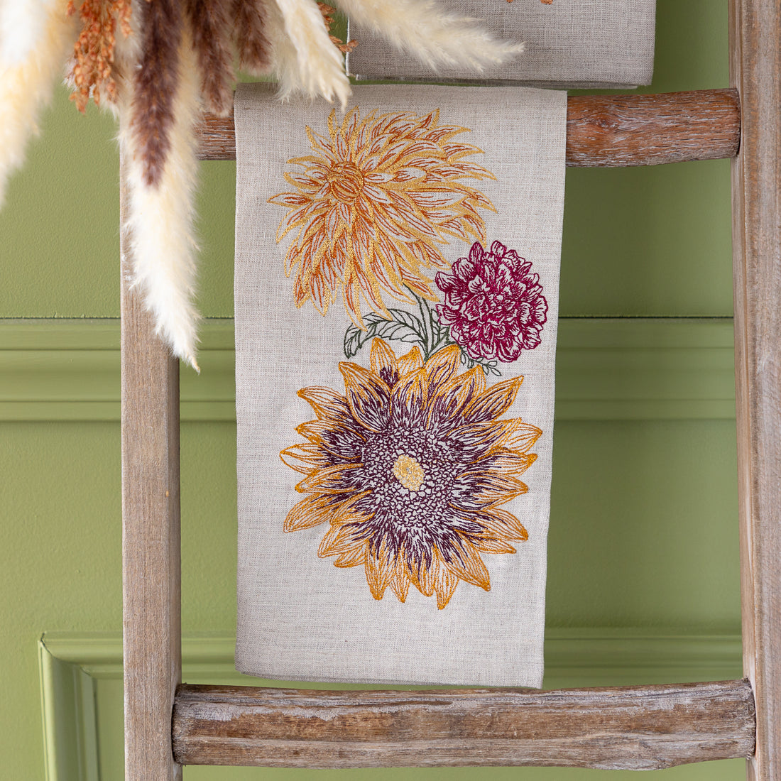 Autumn Sunflower Tea Towel on a wooden ladder against a green wall.