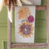 Autumn Sunflower Tea Towel on a wooden ladder against a green wall.