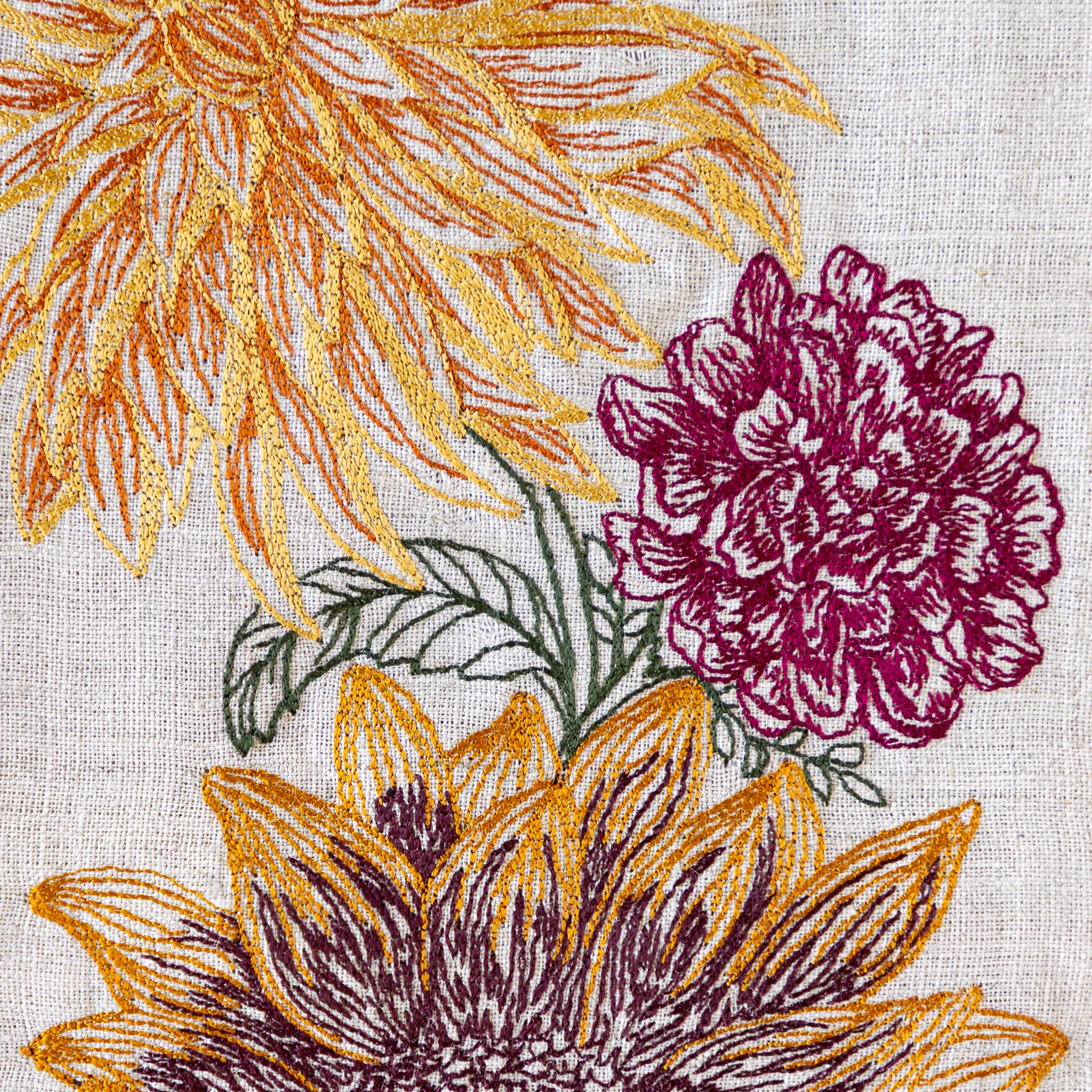 Close-up of embroidered flowers with gold and purple details on a textured fabric background.