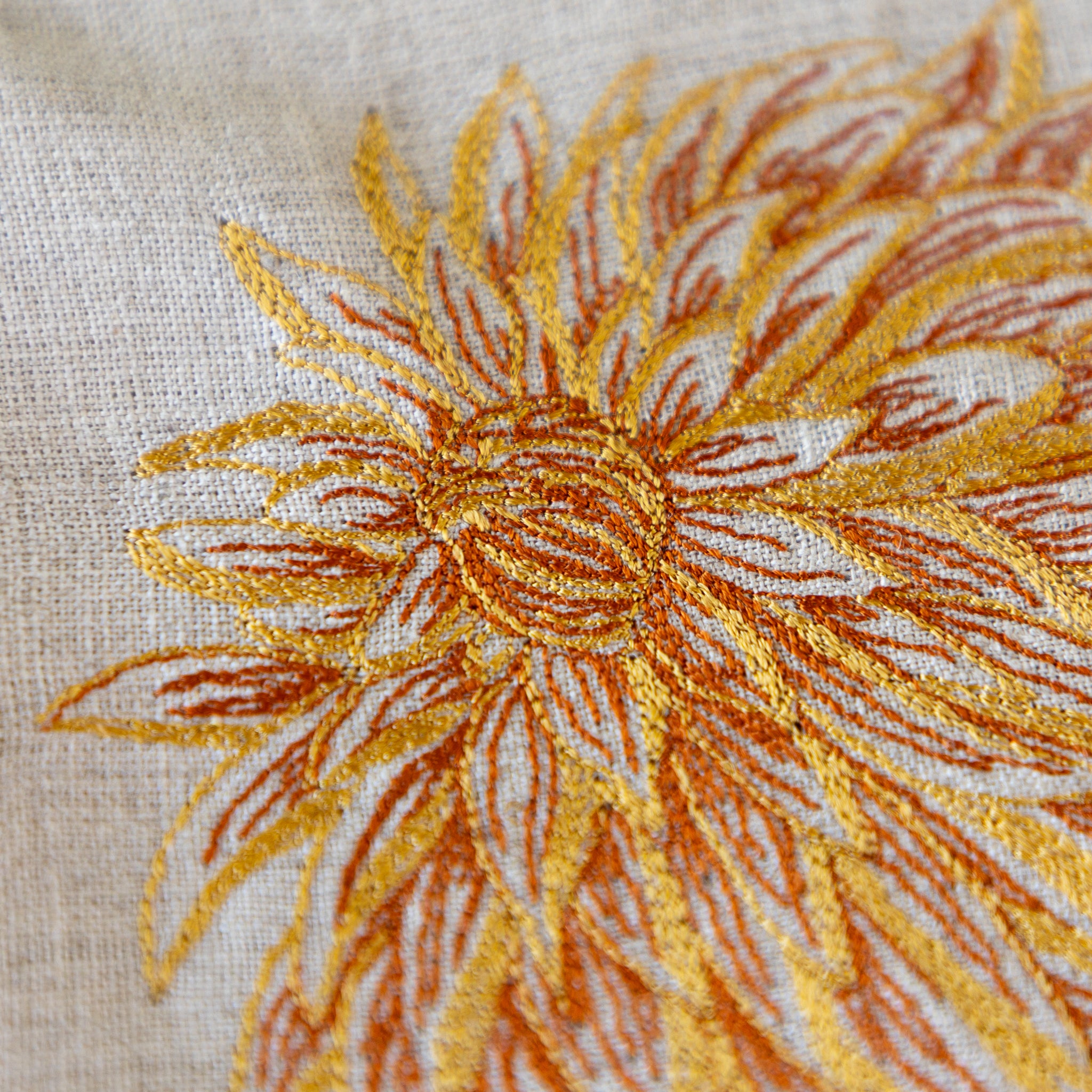 Close-up of a sunflower embroidered on fabric with gold and orange thread.