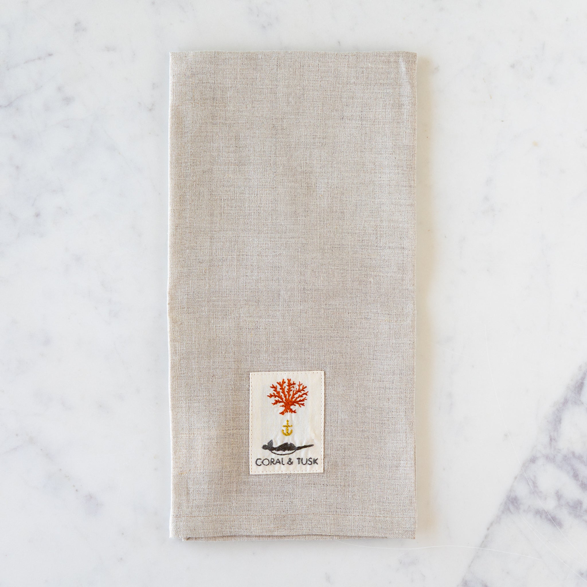 Beige towel with a Coral & Tusk logo on a marble surface.