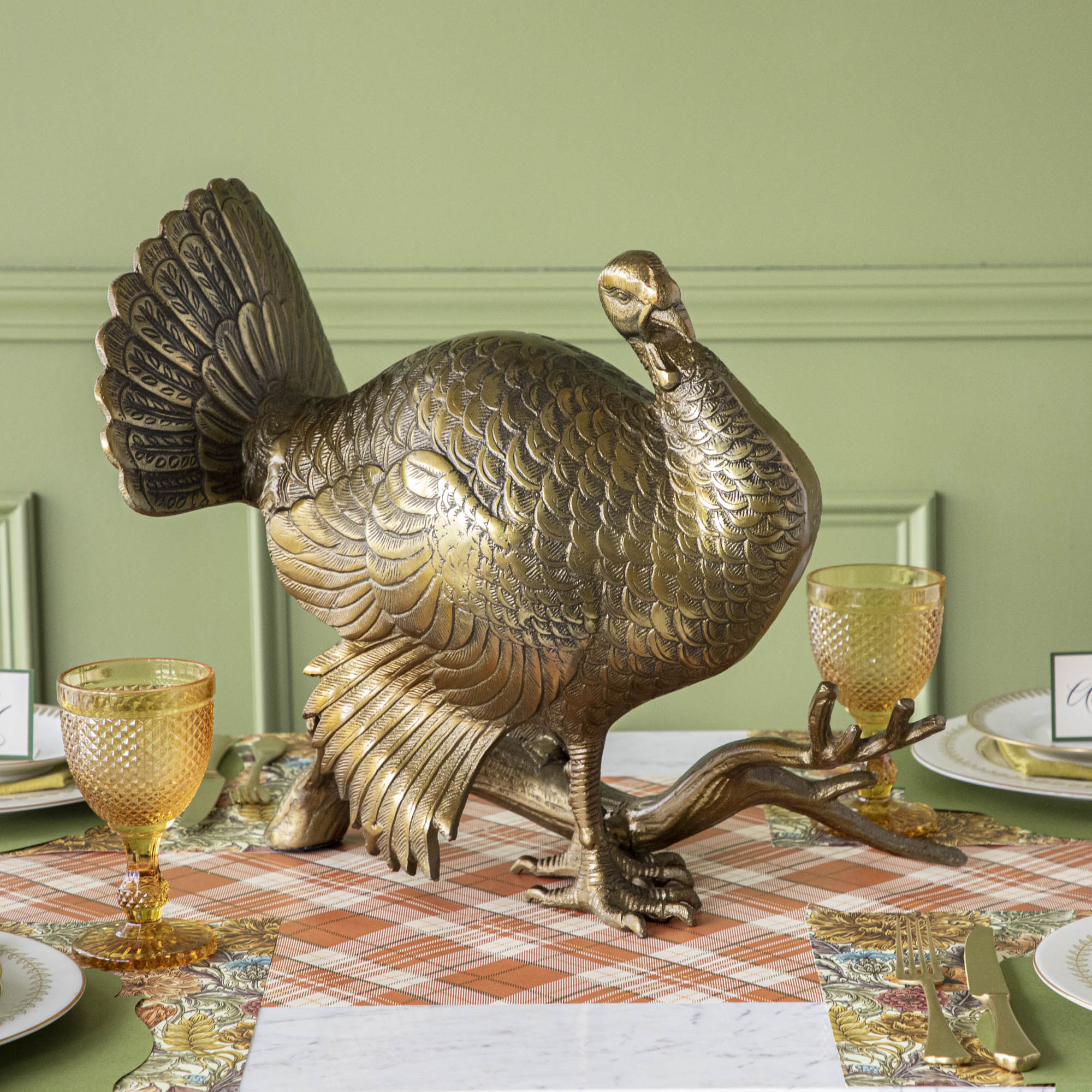 A bronze metal turkey on a branch decoration, placed on a dining table with green wall in the background.