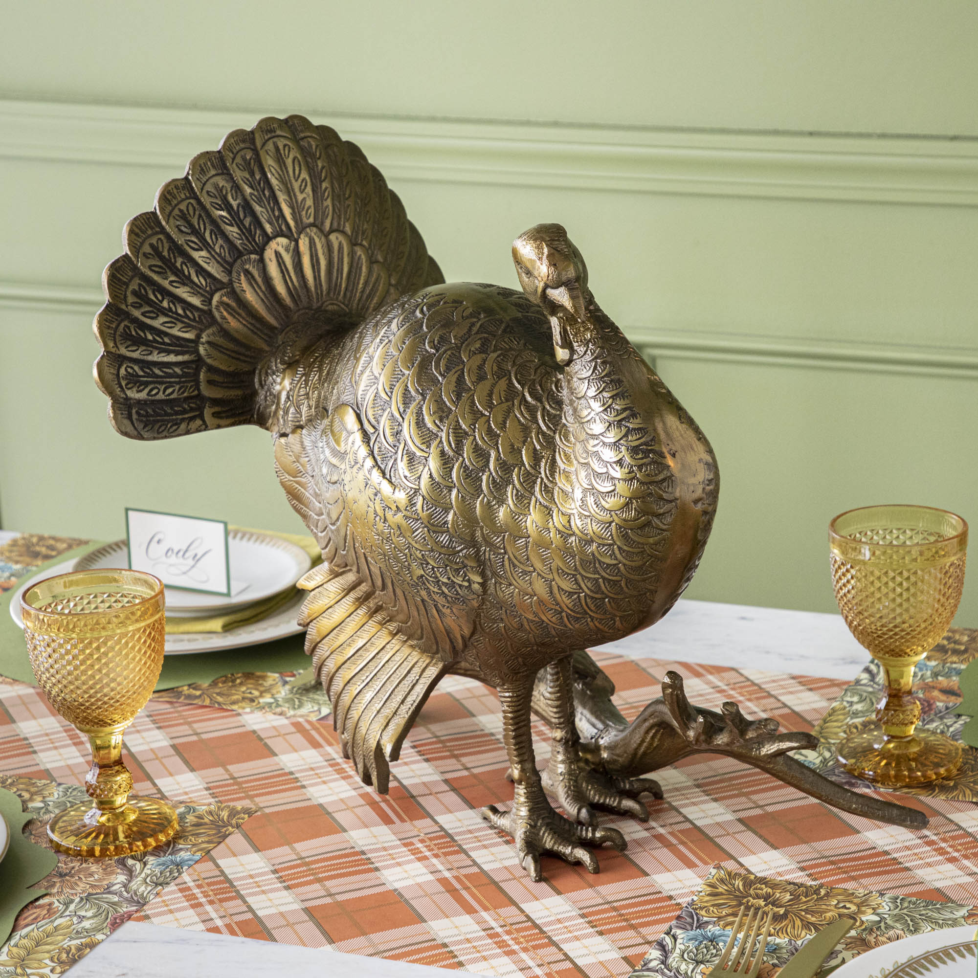 A bronze metal turkey on a branch decoration, placed on a dining table with green wall in the background.
