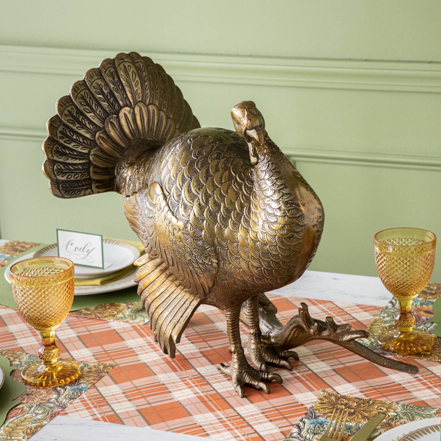 A bronze metal turkey on a branch decoration, placed on a dining table with green wall in the background.