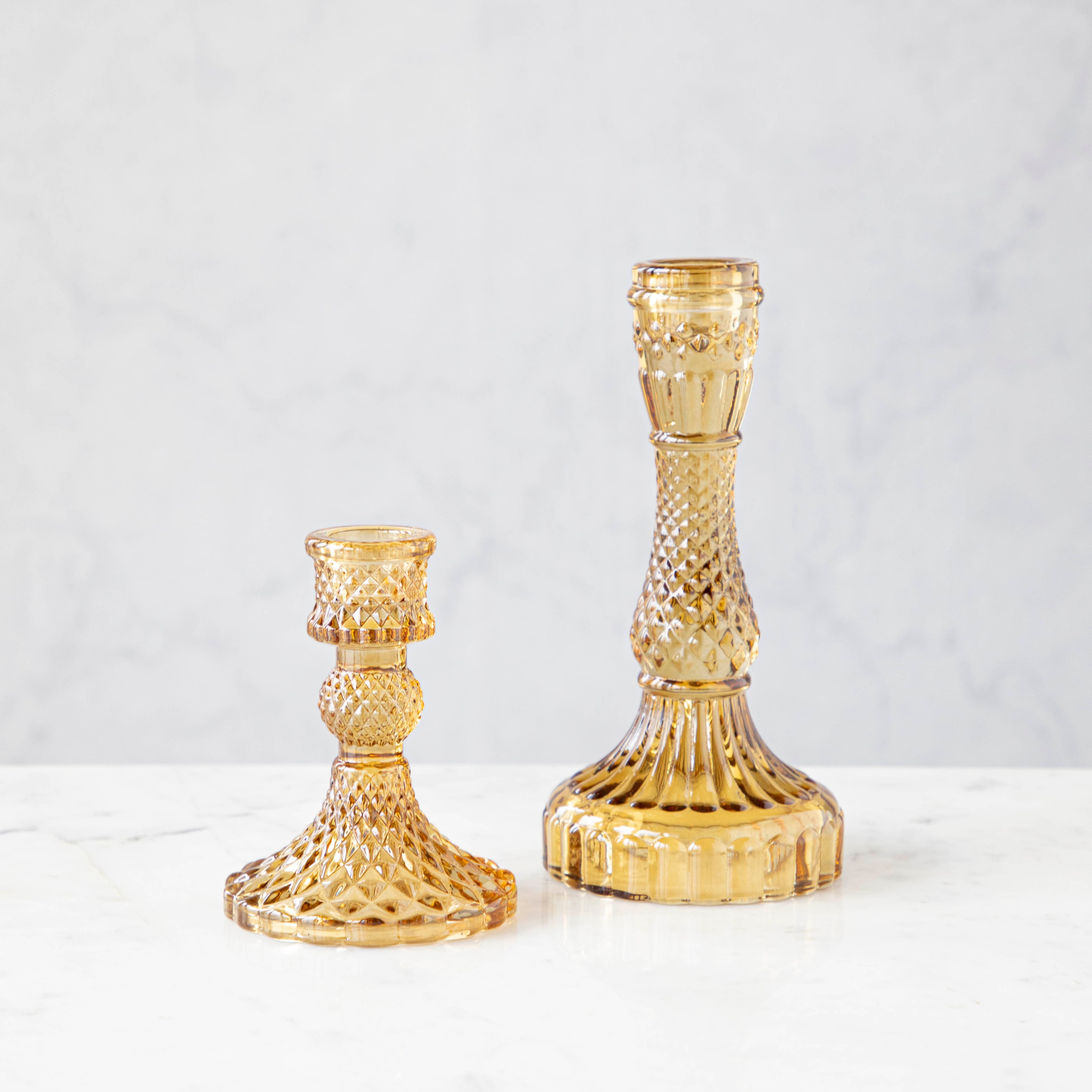 Two amber glass candlesticks of different sizes with a textured design, displayed against a neutral background.