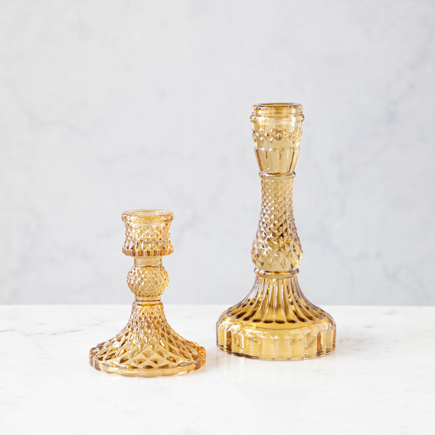 Two amber glass candlesticks of different sizes with a textured design, displayed against a neutral background.