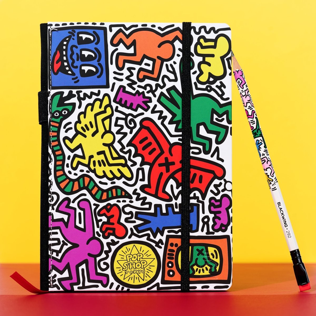 Blackwing notebook with Keith Haring artwork printed on it with a corresponding pencil propped against it.