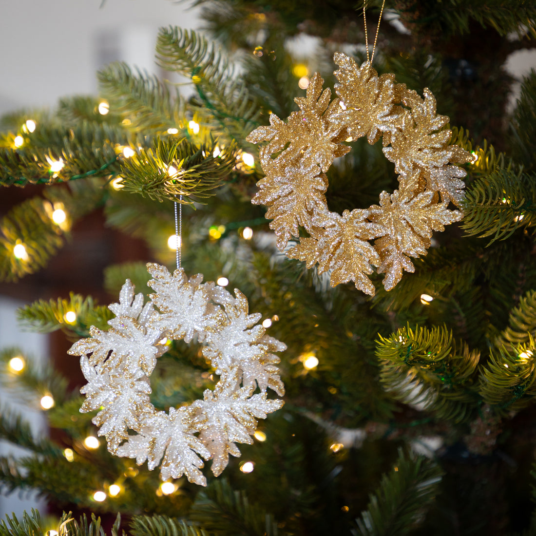 Decorative gold and silver wreath ornaments on a Christmas tree with lights.