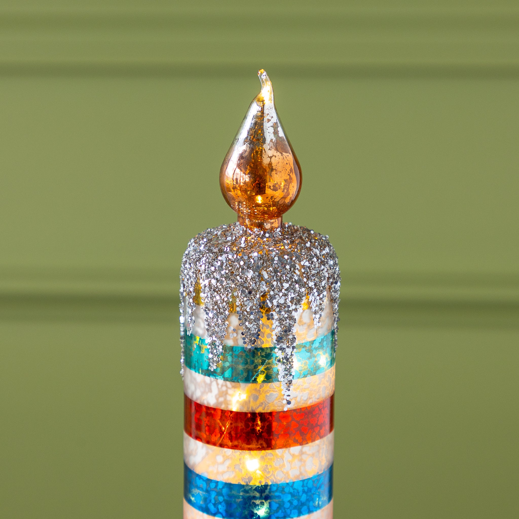 A tabletop candle featuring glittery silver accents and colorful horizontal stripes, this Retro Stripe Glass Candle evokes a mid-century Christmas charm.