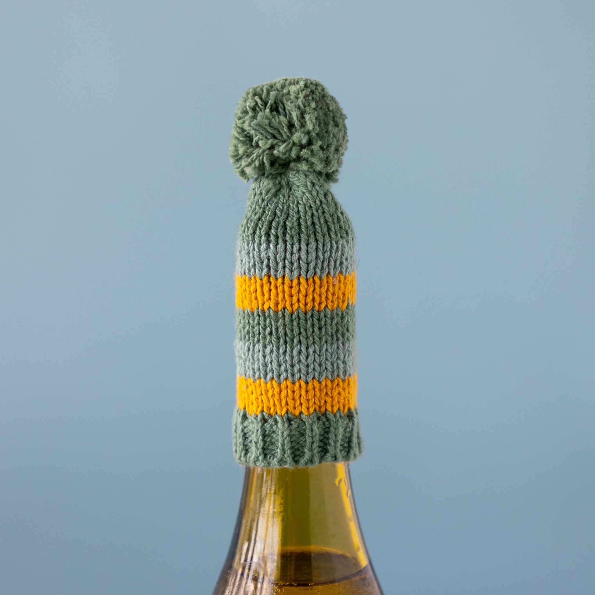 Knitted bottle cover with a pom-pom on a bottle against a blue background.