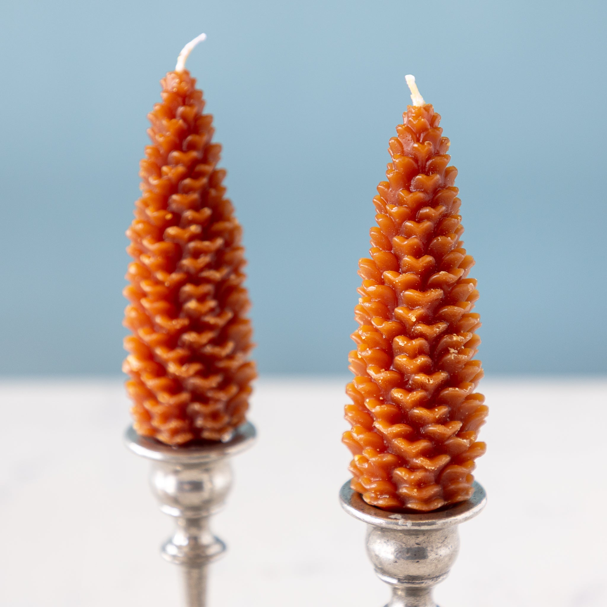 Two cone-shaped beeswax candles on silver candle holders with a light blue background.