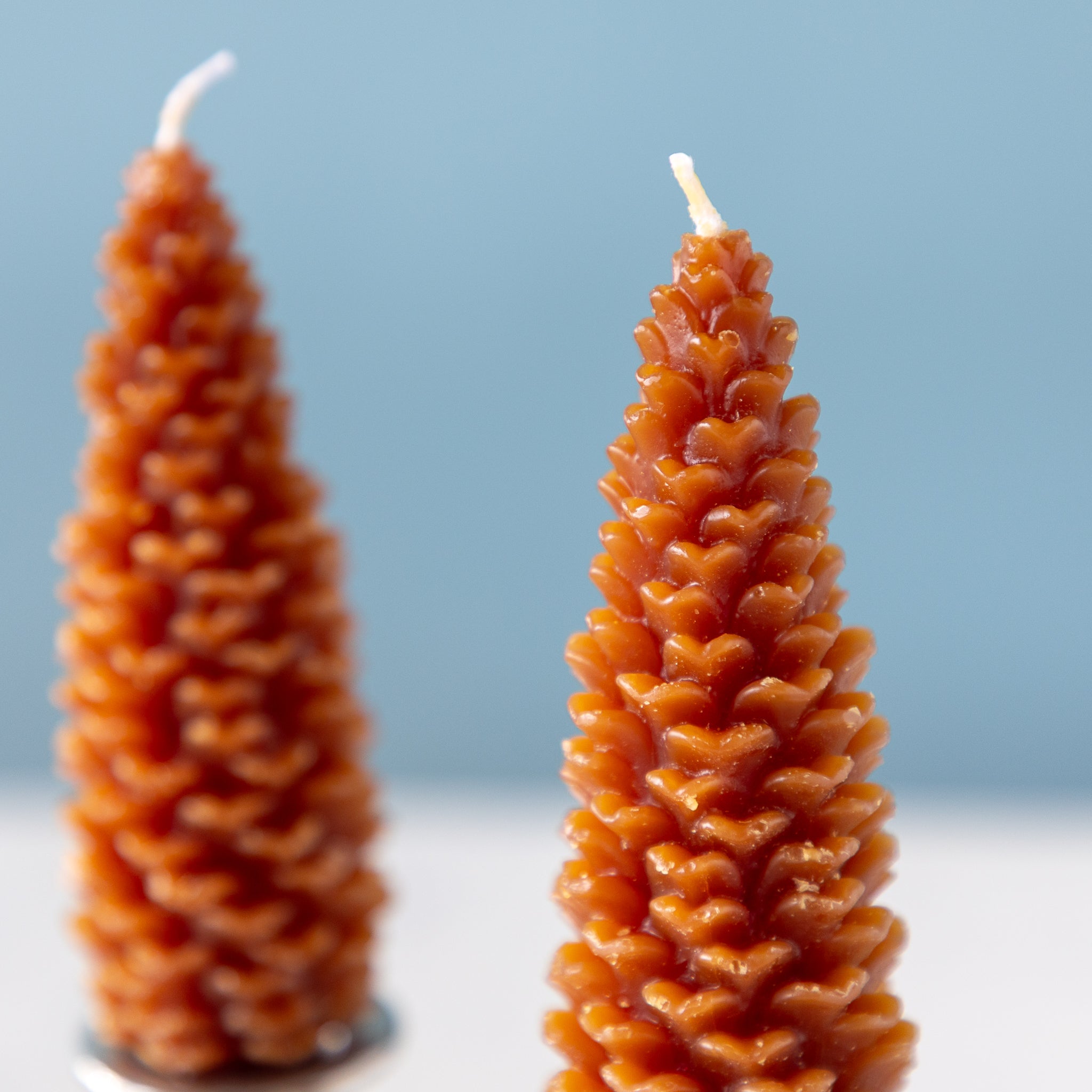 Two cone-shaped candles made of beeswax on a light blue background.