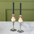 Two Snowman Taper Candles in vintage candlestick holders on a marble table against a green wall.