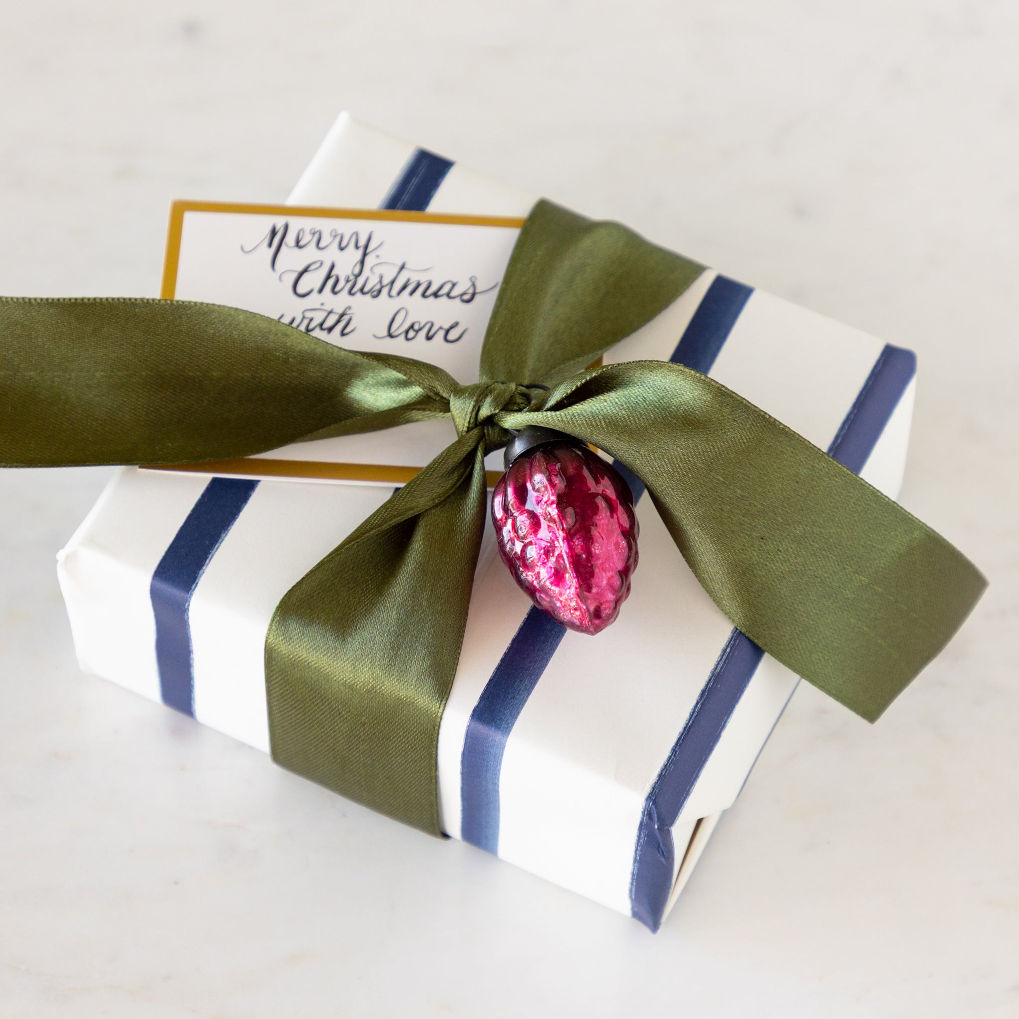 Gift box with green ribbon and pink ornament on a table.