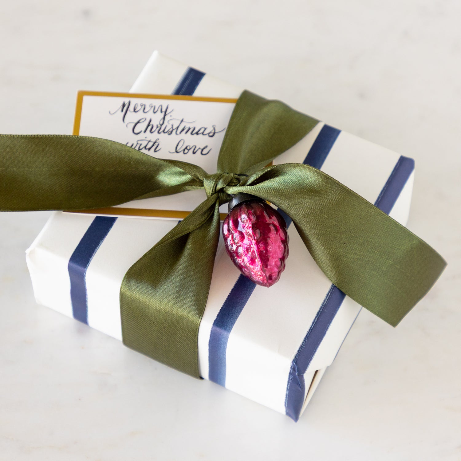 Gift box with green ribbon and pink ornament on a table.
