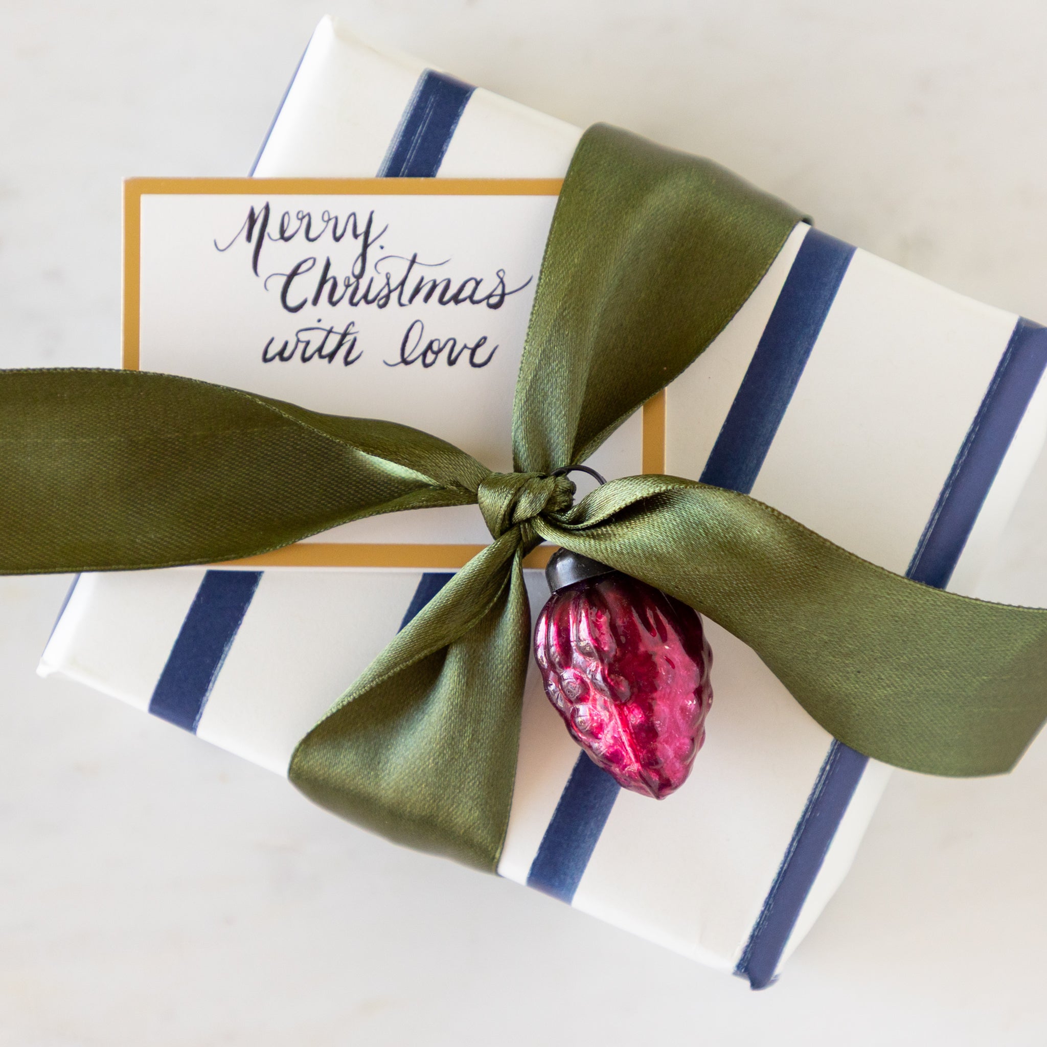 Gift box with green ribbon and pink ornament on a table.