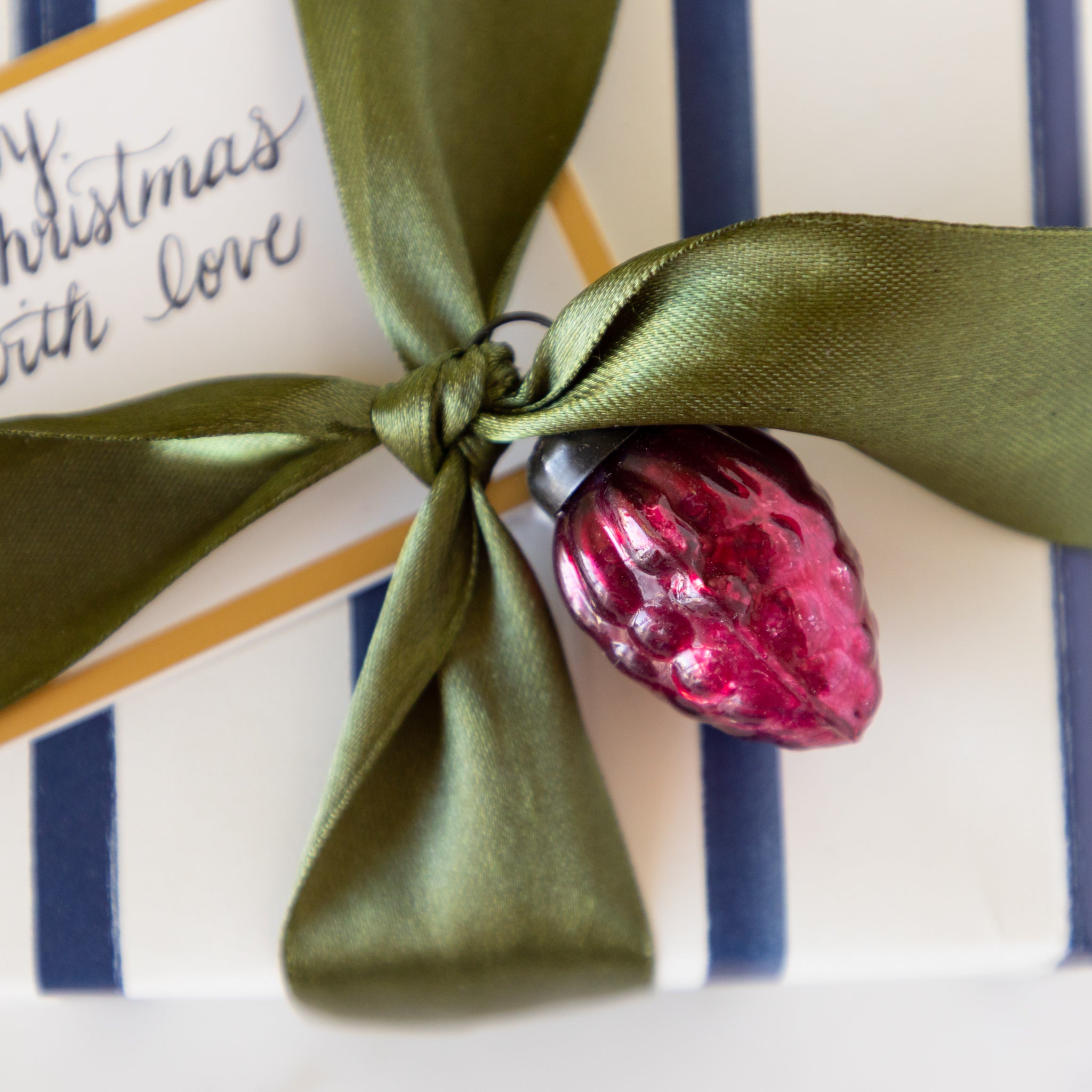 Gift box with green ribbon and pink ornament on a table.