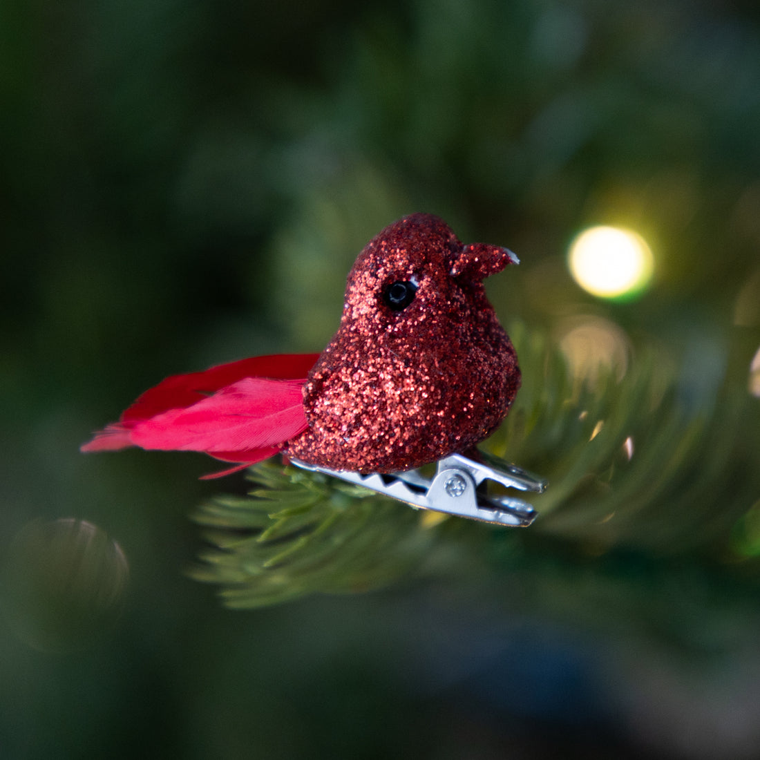 Red glittery bird ornament on a branch with blurred green background.