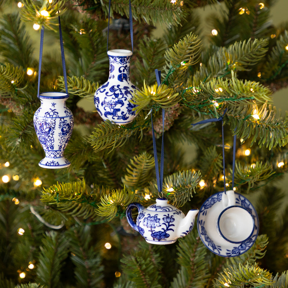 Decorative blue and white teapot, teacup, and vase ornaments hanging on a Christmas tree.