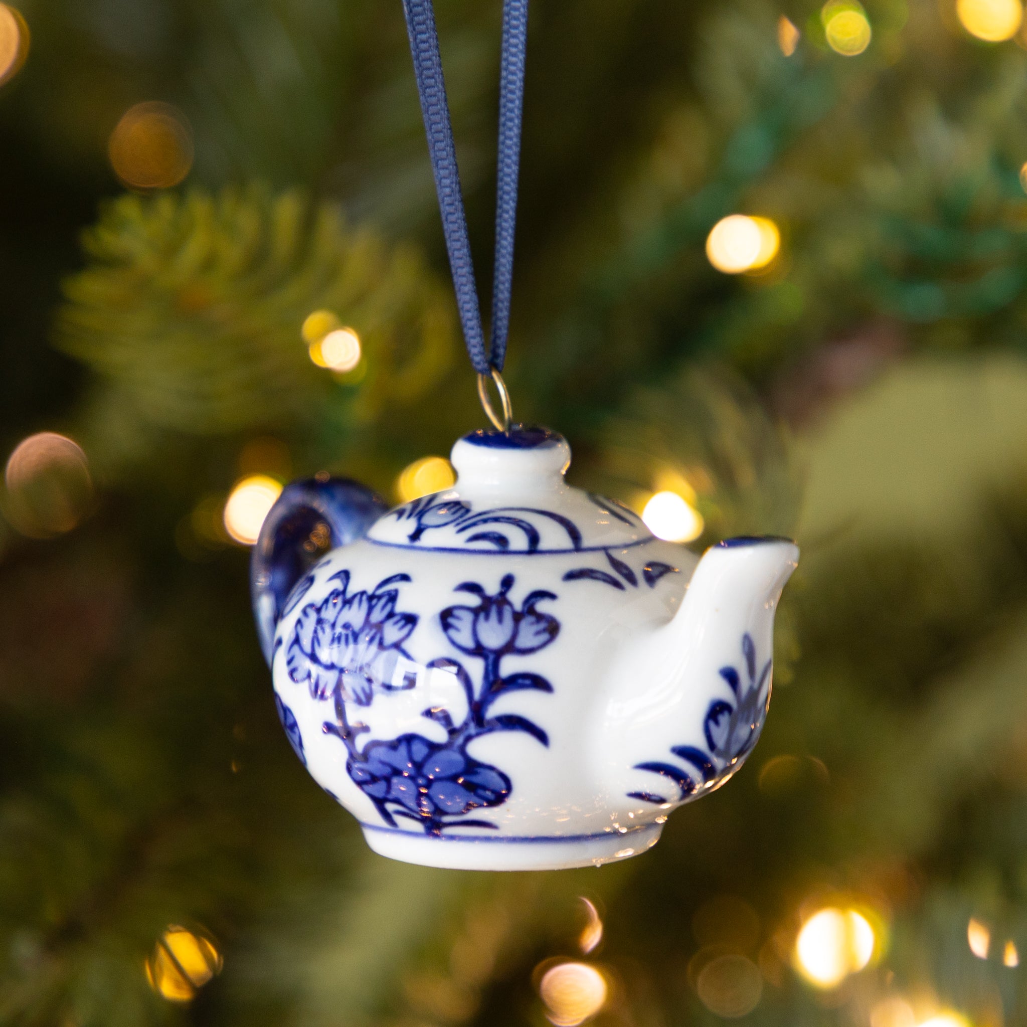Decorative teapot ornament with blue floral patterns hanging on a Christmas tree.