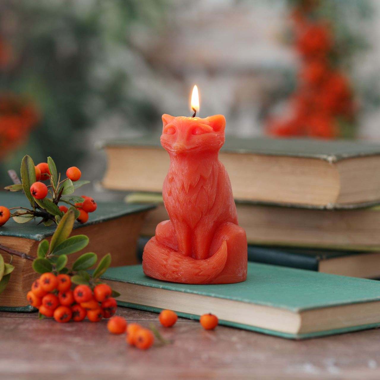 Candle shaped like a fox on books with berries and leaves in the background