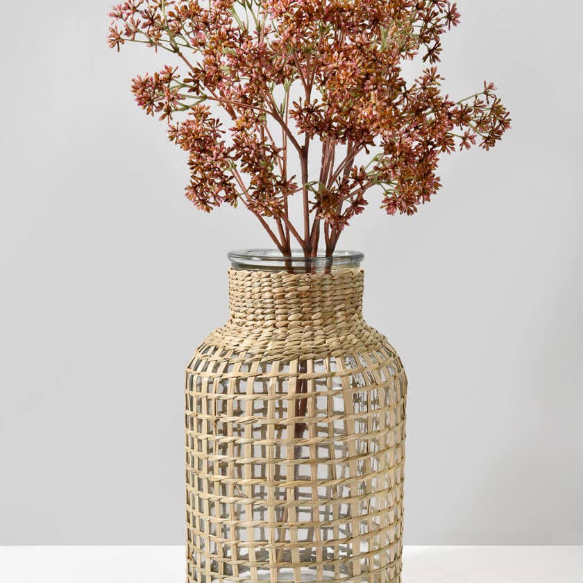 Woven rattan vase with dried flowers on a light gray background.