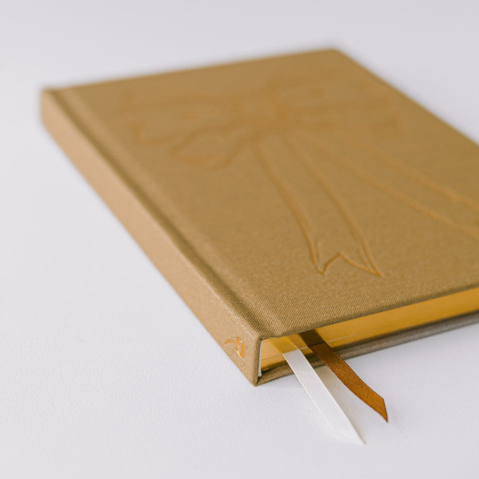 Notebook by Good Juju with gold detailing depicting a bow. 