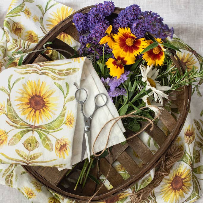 Basket with flowers, scissors, and fabric on a floral-patterned surface