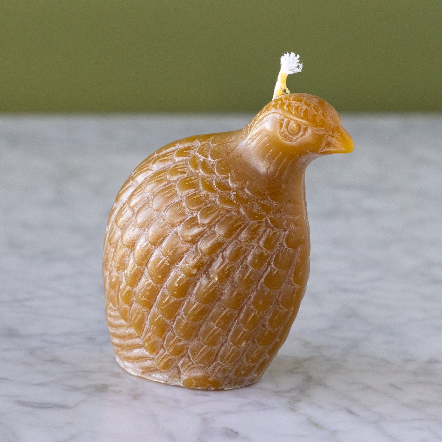 A Partridge Beeswax candle in amber and on a marble surface with a green wall background.