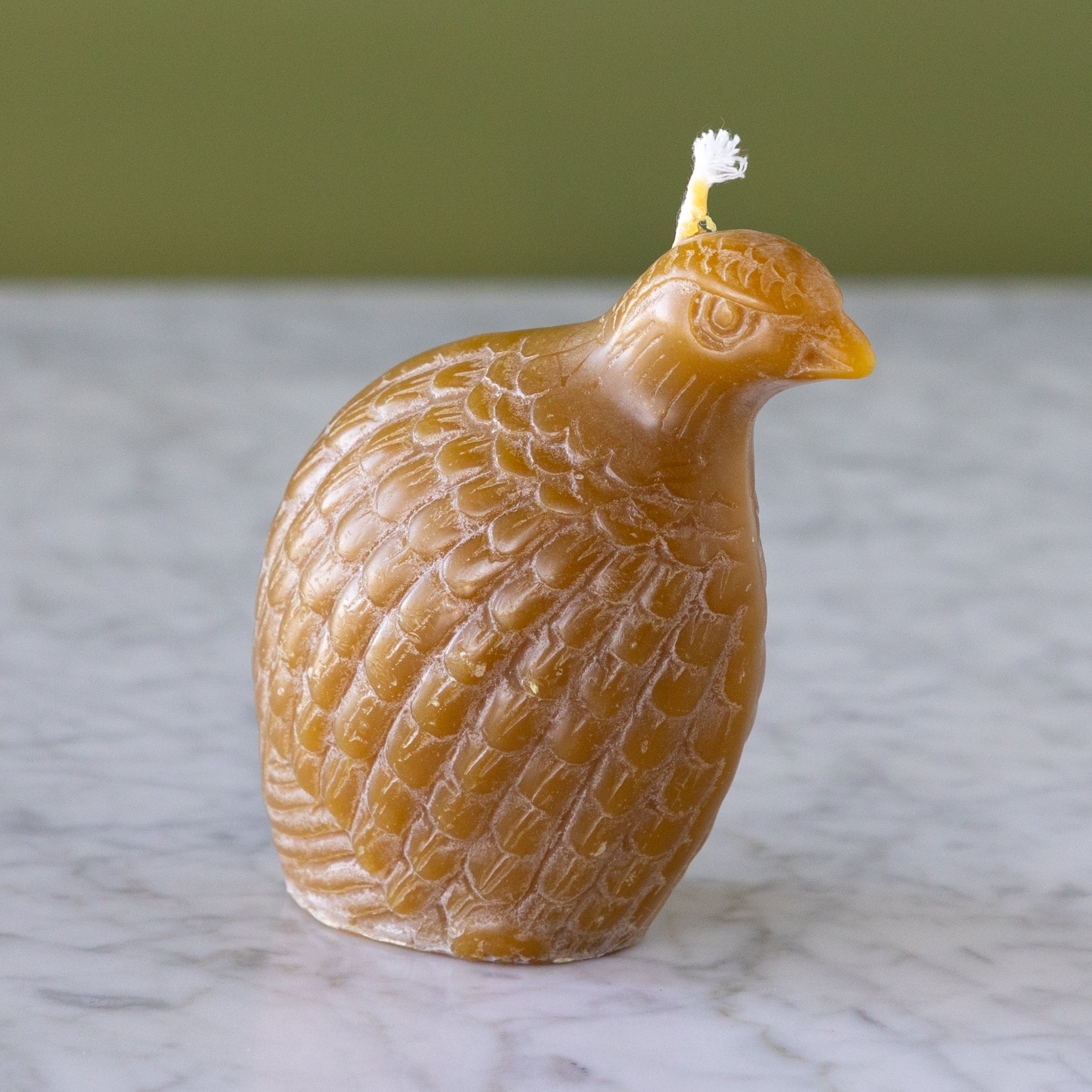 A Partridge Beeswax candle in amber and on a marble surface with a green wall background.