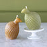 Two Partridge Beeswax candles, one amber and one sage on a marble surface with a green wall background.
