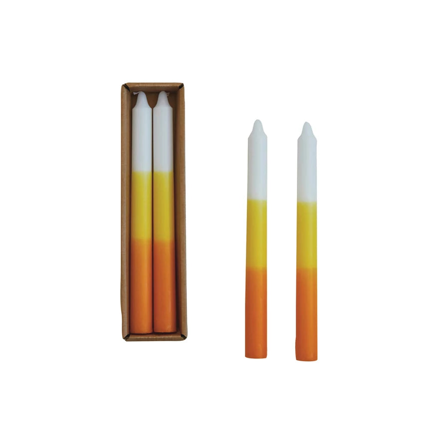 A set of two taper candles with yellow, orange, and white coloring, presented in a box.