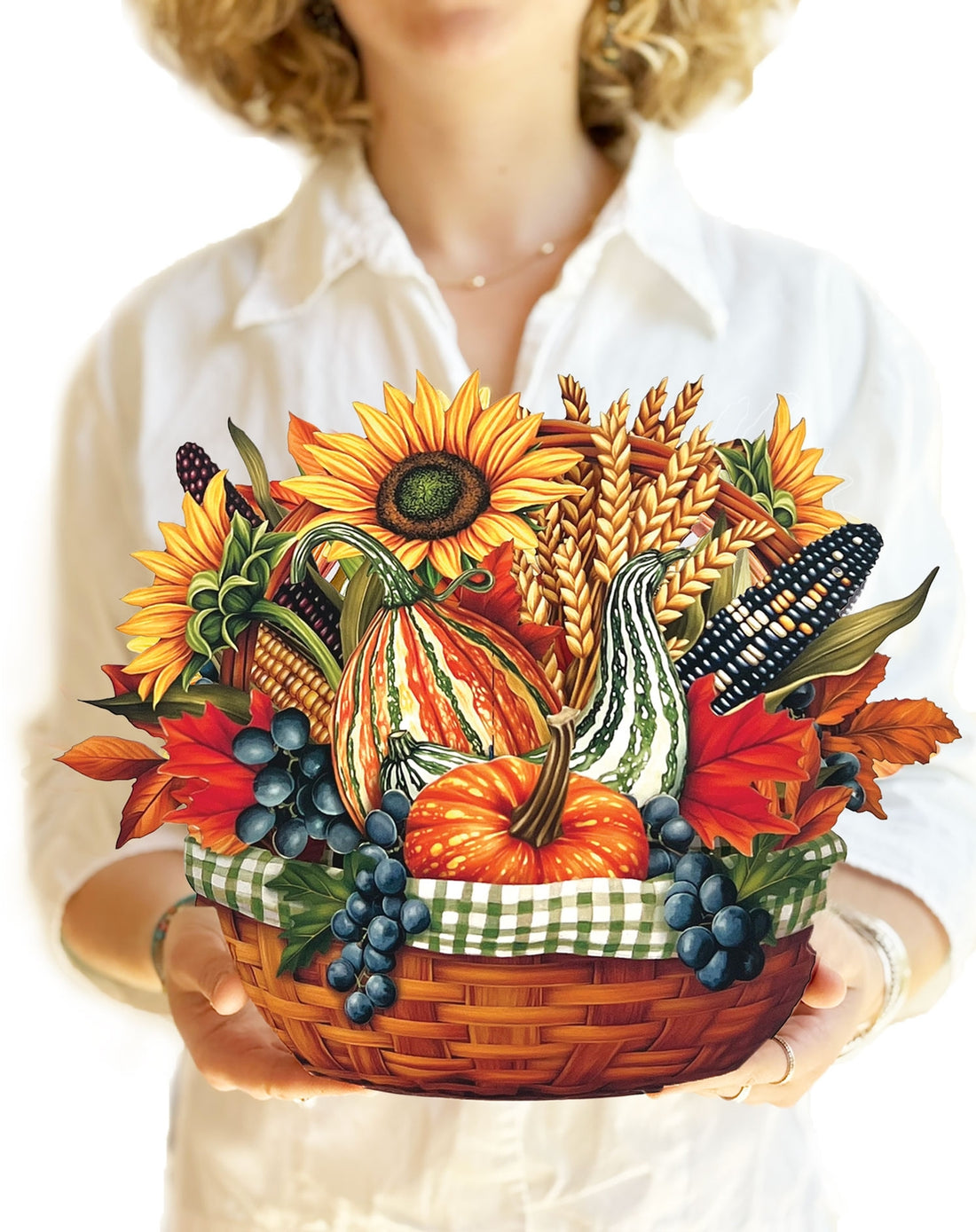 Person holding a paper decorative basket with autumn-themed items including pumpkins, sunflowers, and corn.