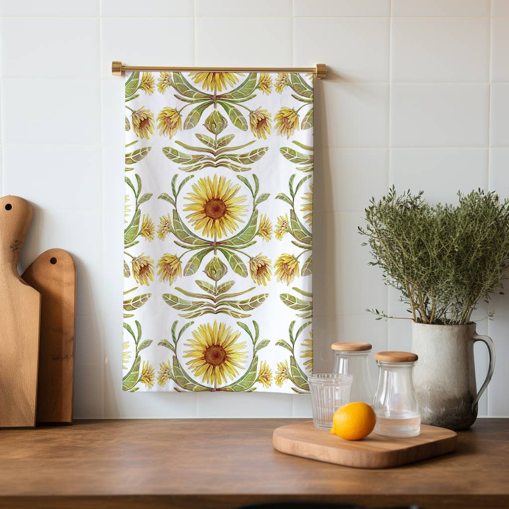 Decorative sunflower patterned towel hanging on a wooden rod above a kitchen counter with cutting boards and a vase.