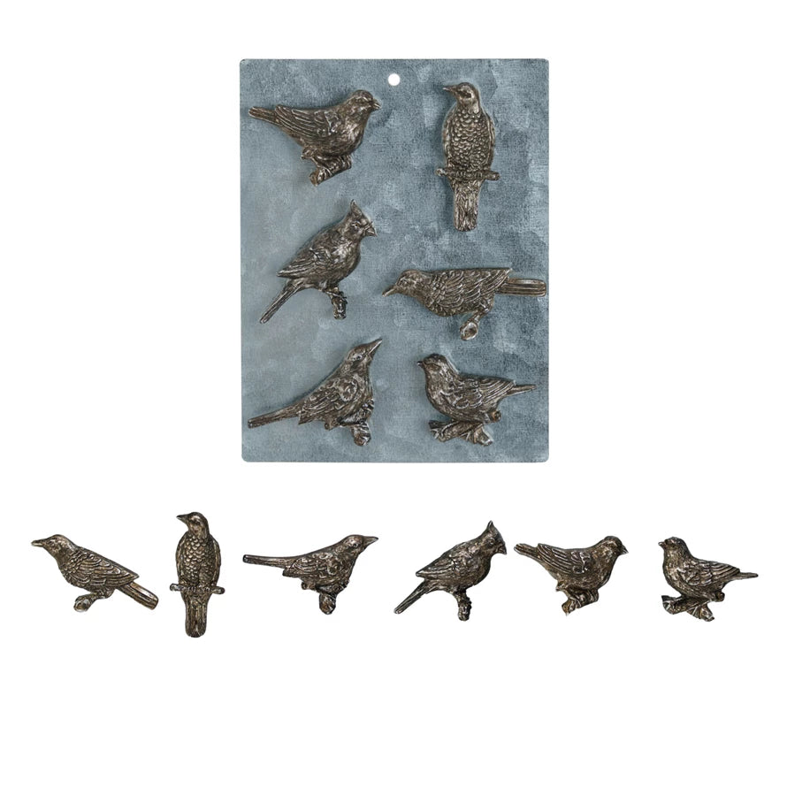 A collection of pewter bird-shaped magnets displayed on a surface.