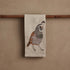 Towel with a quail design hanging on a wooden rod against a beige wall.