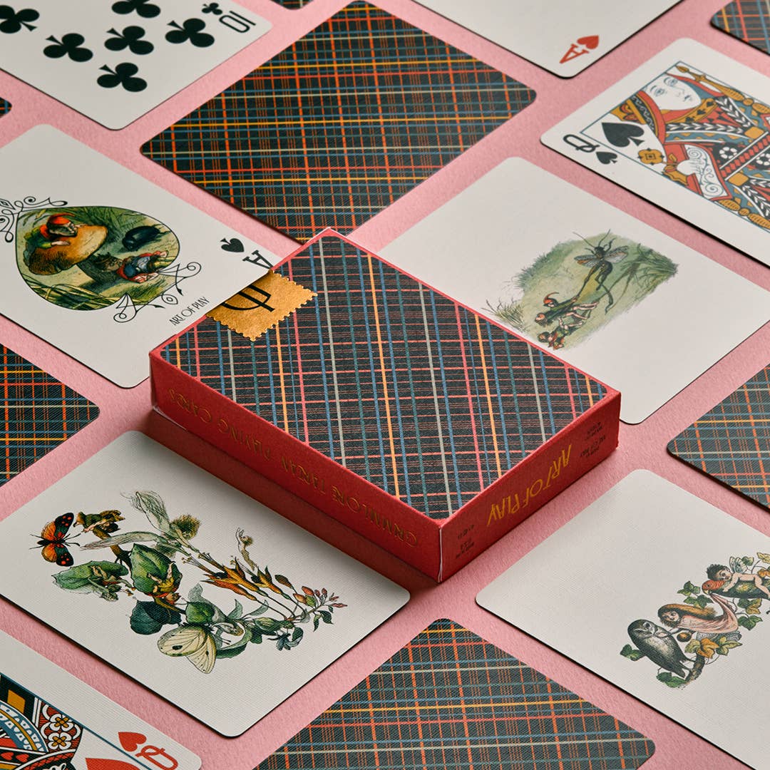 Playing cards with decorative designs on a pink surface, with a red card holder in the center.