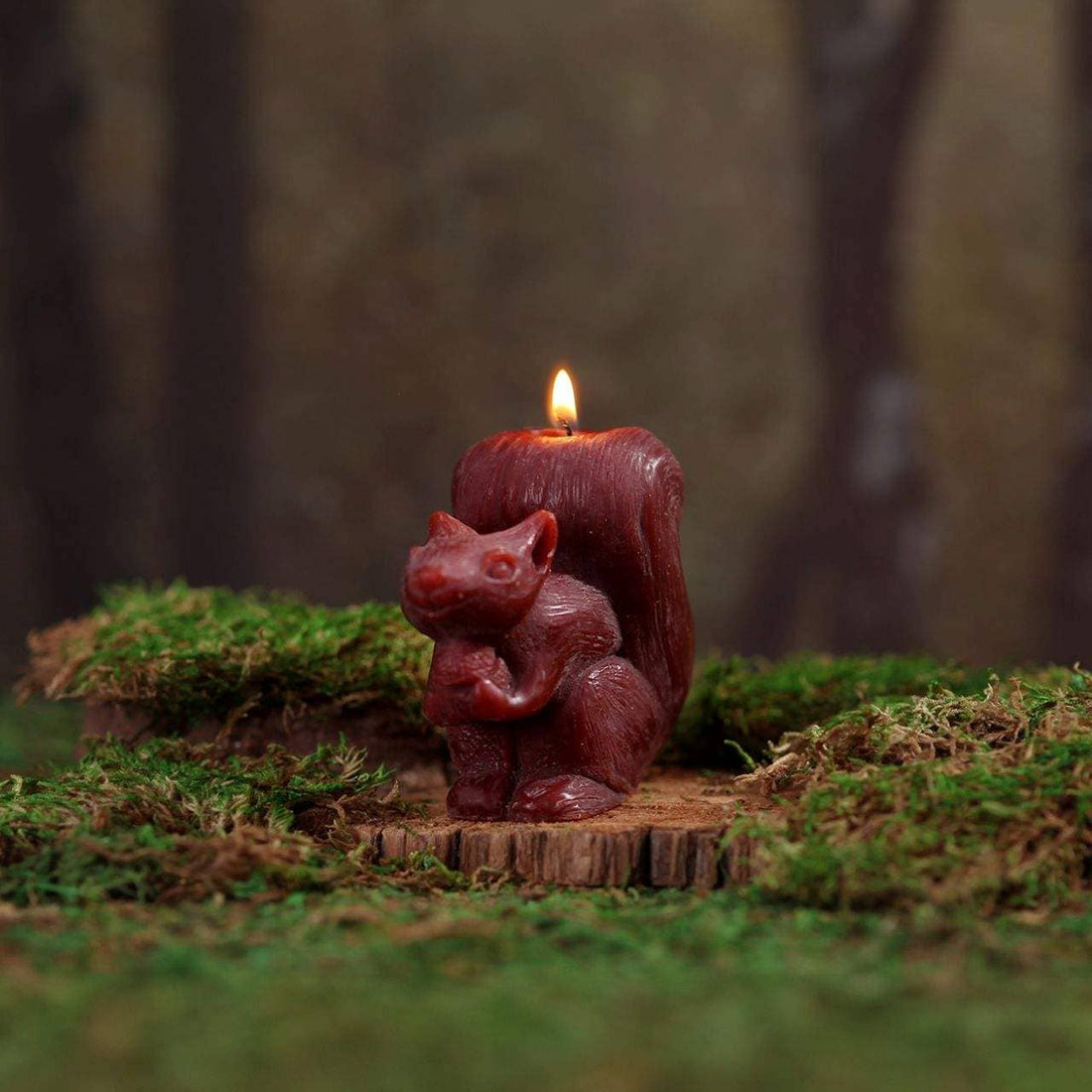 Squirrel-shaped candle on a wooden stump with a blurred forest background